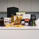 The Gluten-Free Gourmet Delights Hamper. A neatly arranged tabletop featuring a variety of food items. There is a loaf of bread, bags of chips, jars of spreads, and boxes of snacks. The background includes minimalist kitchen cabinetry. The Gluten-Free Gourmet Delights Hamper. A neatly arranged tabletop featuring a variety of food items. There is a loaf of bread, bags of chips, jars of spreads, and boxes of snacks. The background includes minimalist kitchen cabinetry.